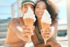 Zwei junge Frauen lächeln fröhlich und halten Eis in die Kamera.